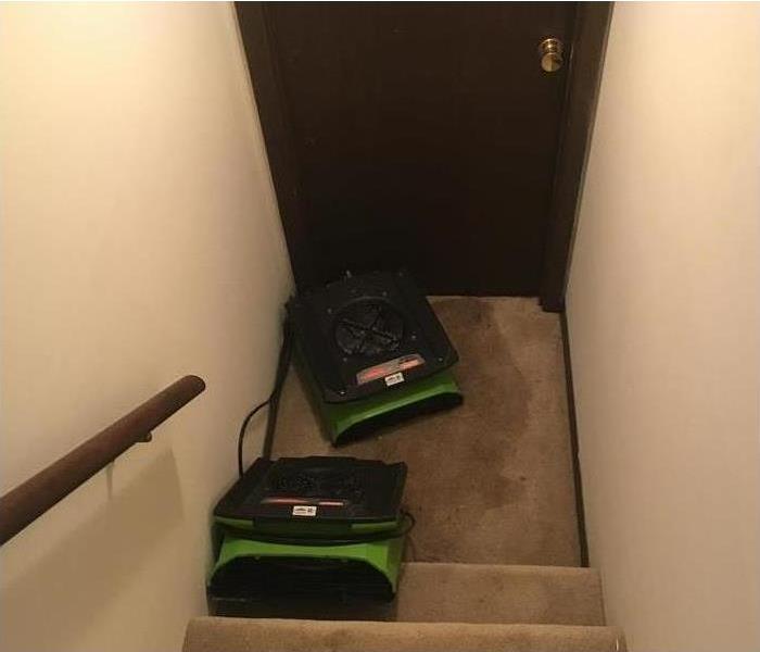 Two air movers placed on stairs with wet carpet floor.