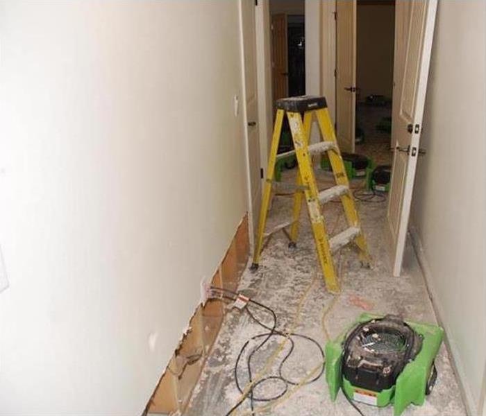 Flood cut performed on drywall, latter and an air mover in the hallway of a home