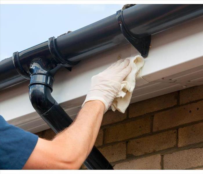 Man cleaning and maintaining plastic guttering on a house