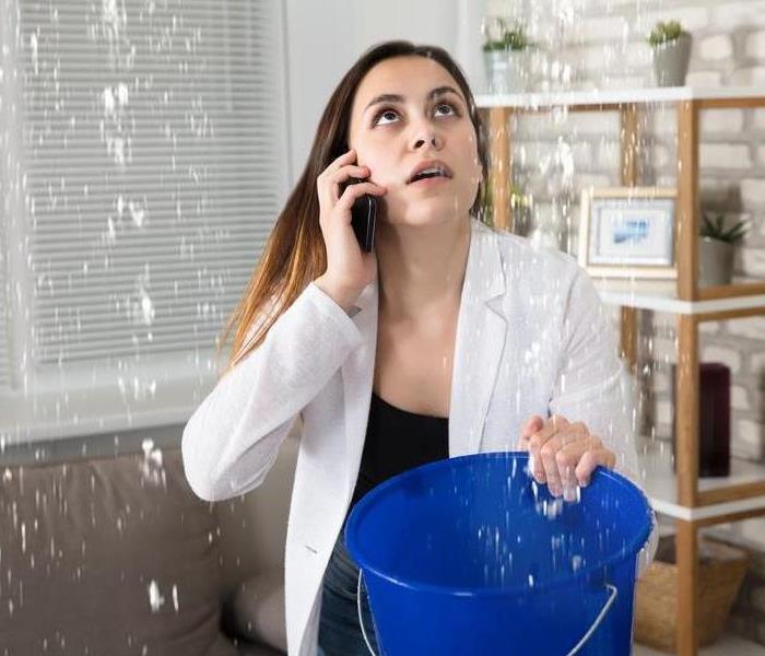 Woman calling while collecting water droplets leaking from ceiling at home